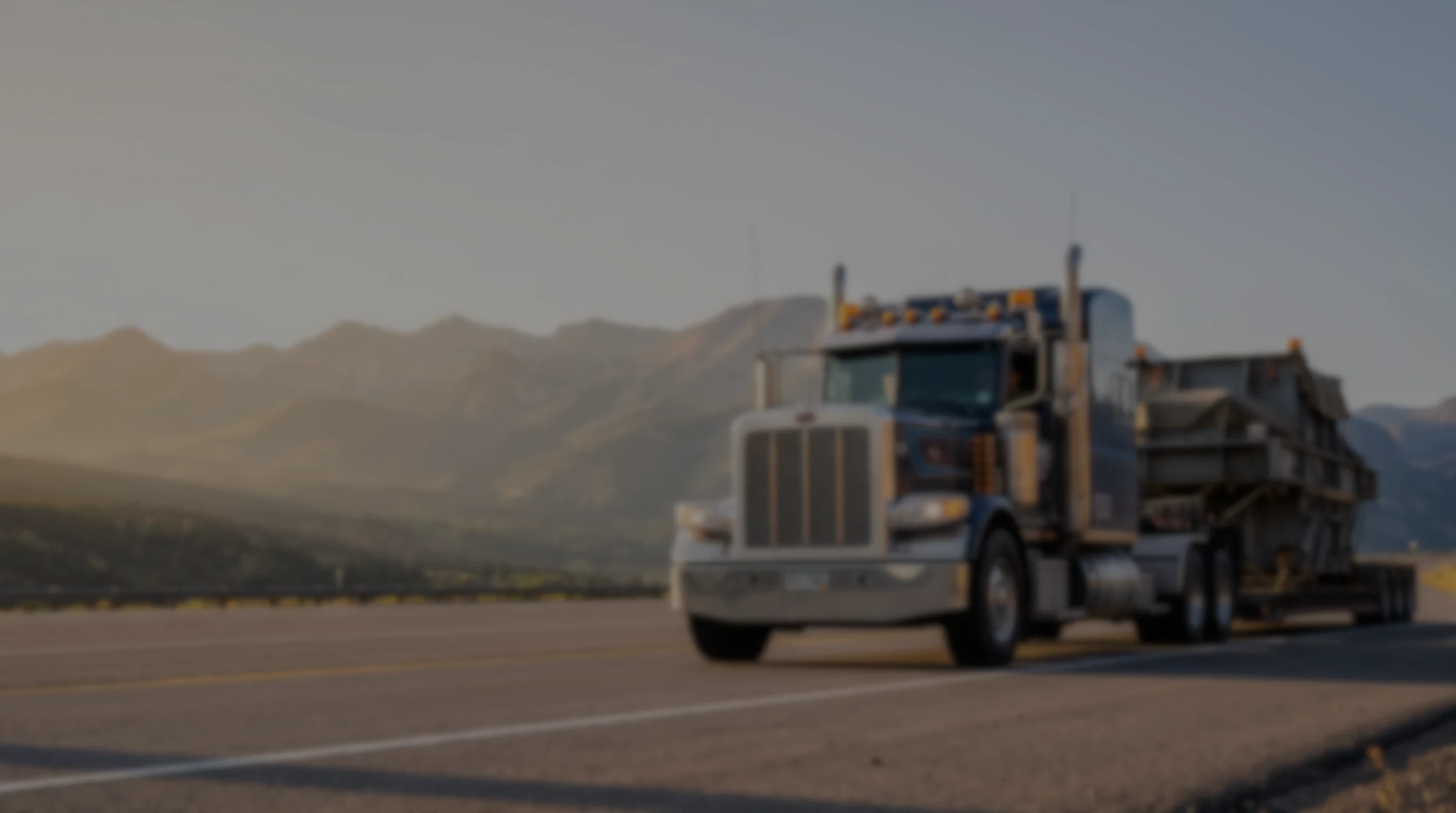 Heavy-haul truck carrying an oversized industrial load down a mountain highway at golden hour